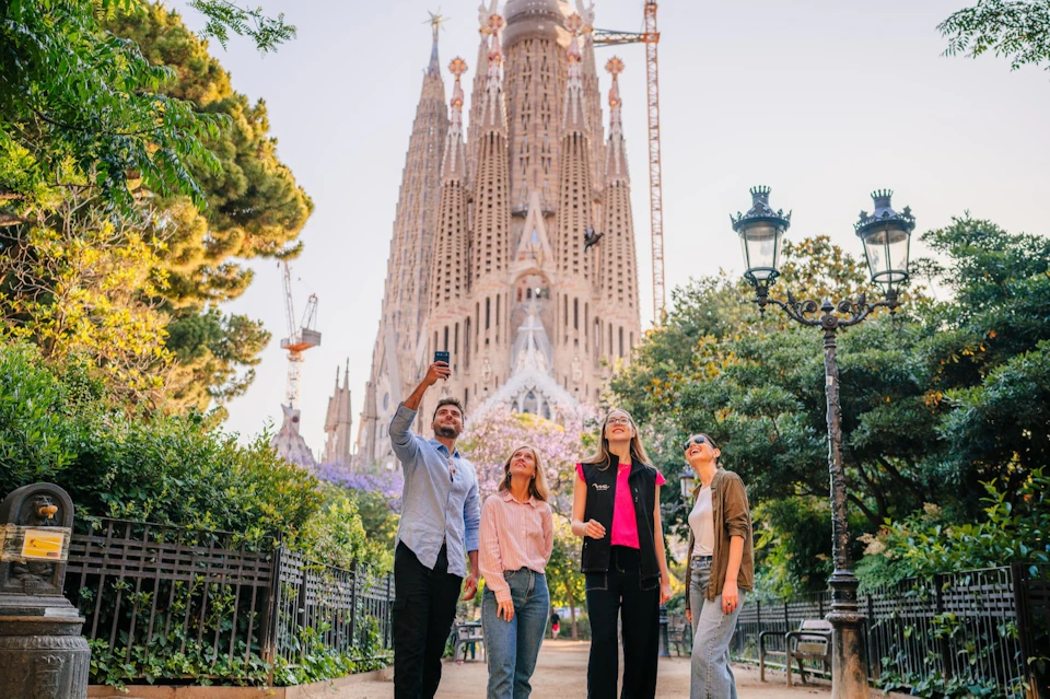 Four people stand in front of the Sagrada Familia cathedral, with one holding up a phone for a selfie.