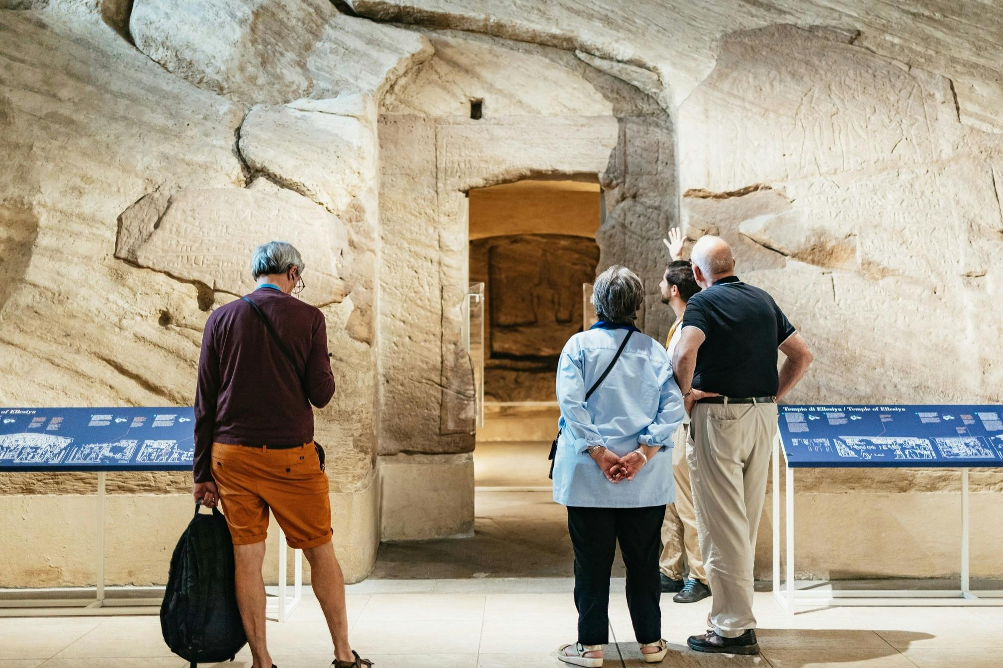 Four people stand in front of a stone archway in a museum, observing and discussing the exhibit.