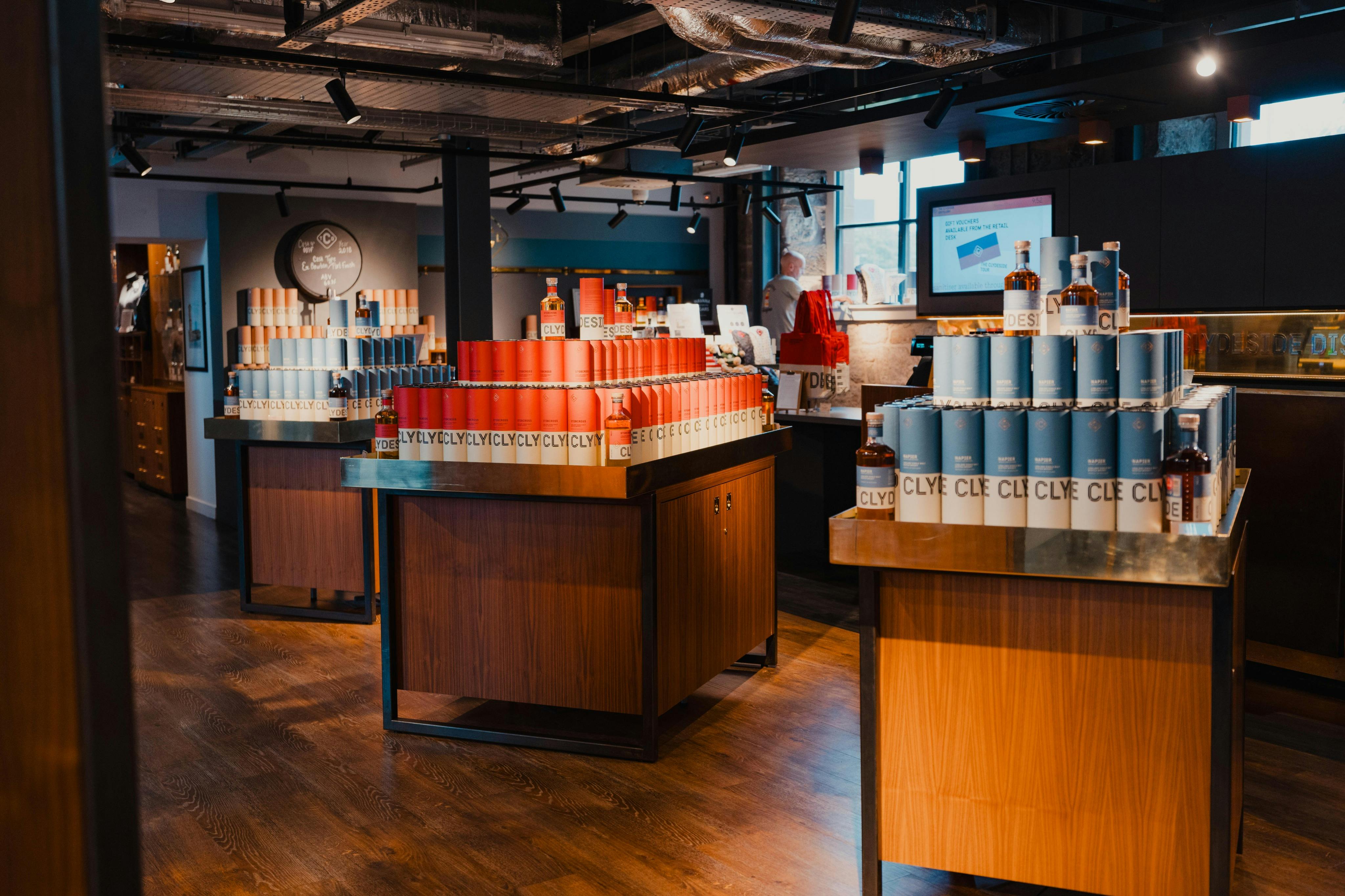 Butiksinteriør med displayborde i træ, der viser rækker af cylindriske produktpakker i blå og røde farver.