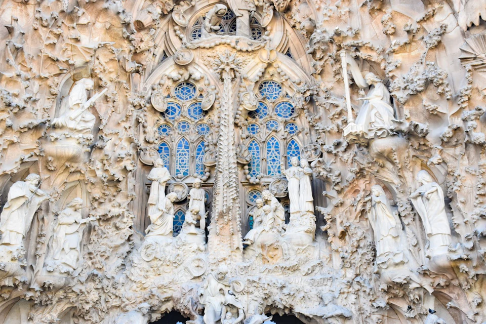 Detailed facade of a cathedral featuring intricate stone carvings, statues of biblical figures, and stained glass windows.