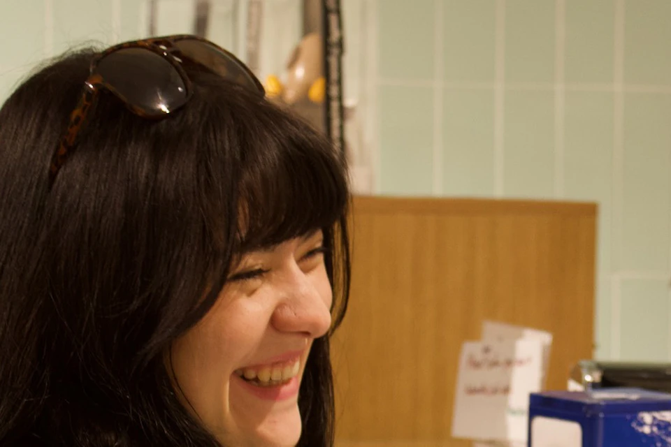 A woman smiling while reaching for something at a counter in a shop, with two men in the background assisting.