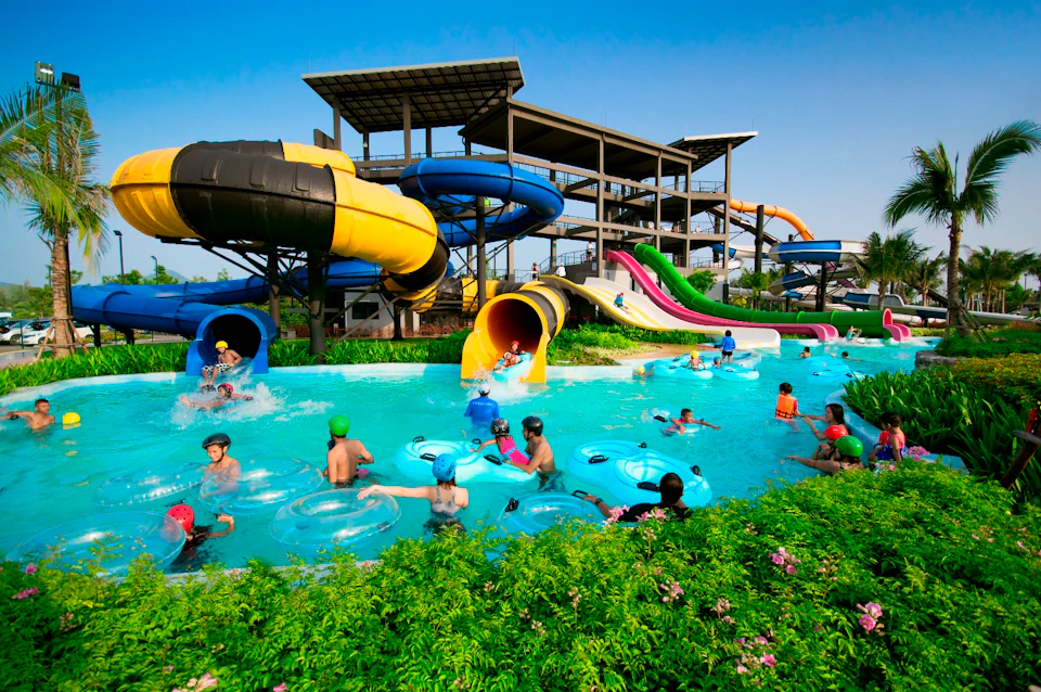 People enjoying a water park, featuring colorful water slides and a lazy river with individuals on inflatable tubes.