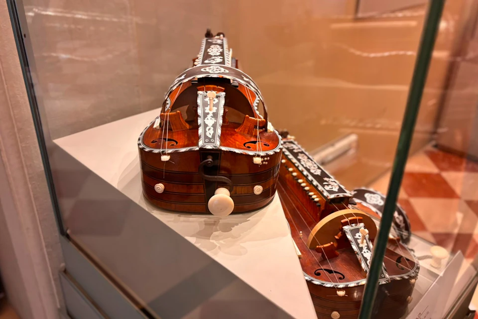 A close-up view of a hurdy-gurdy instrument with intricate inlays, displayed in a well-lit glass showcase.