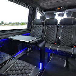 Interiören i en lyxig skåpbil med svarta lädersäten, ett fällbart bord och blå accentbelysning, sedd genom ett stort fönster.