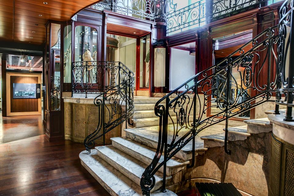 Elegant marble staircase with intricate wrought iron railings in a luxurious, wood-paneled interior featuring large mirrors.