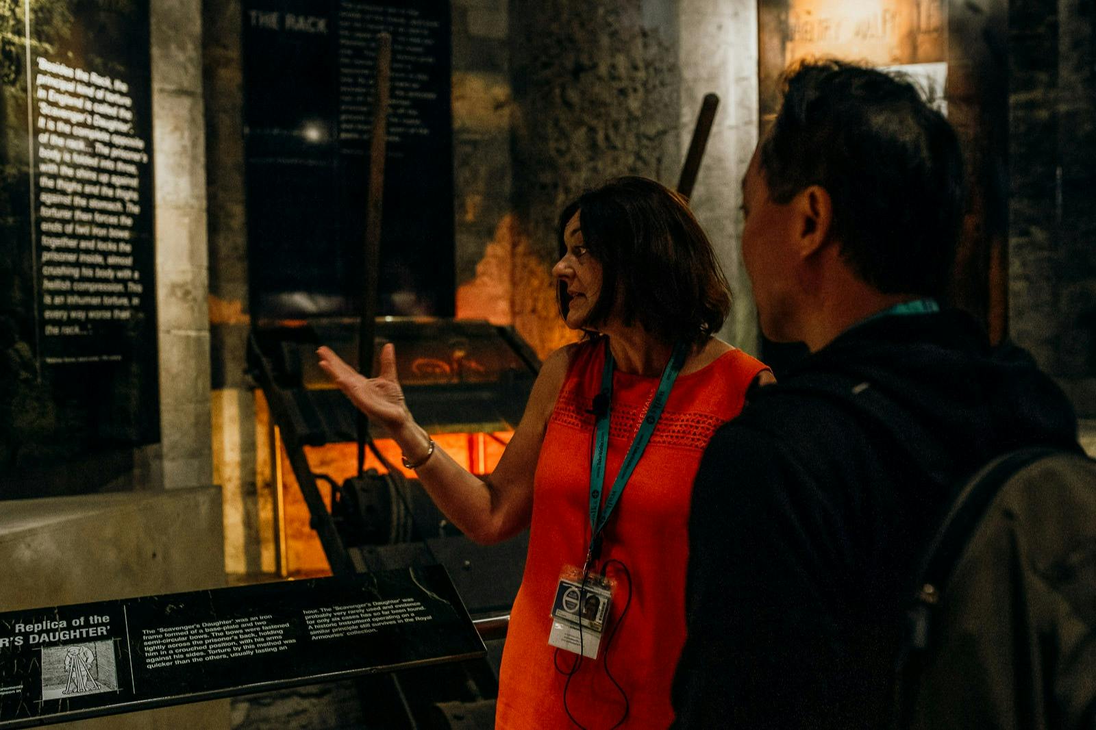 A woman in an orange dress giving a tour to a man, with historical exhibits and information panels in the background.