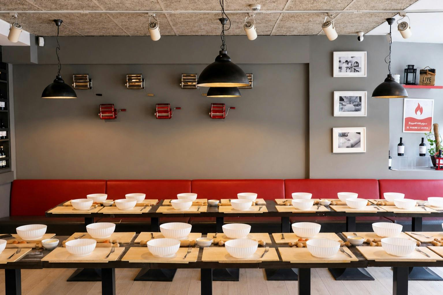 A restaurant interior with neatly set tables featuring white bowls and utensils, red bench seating, and wall decorations.