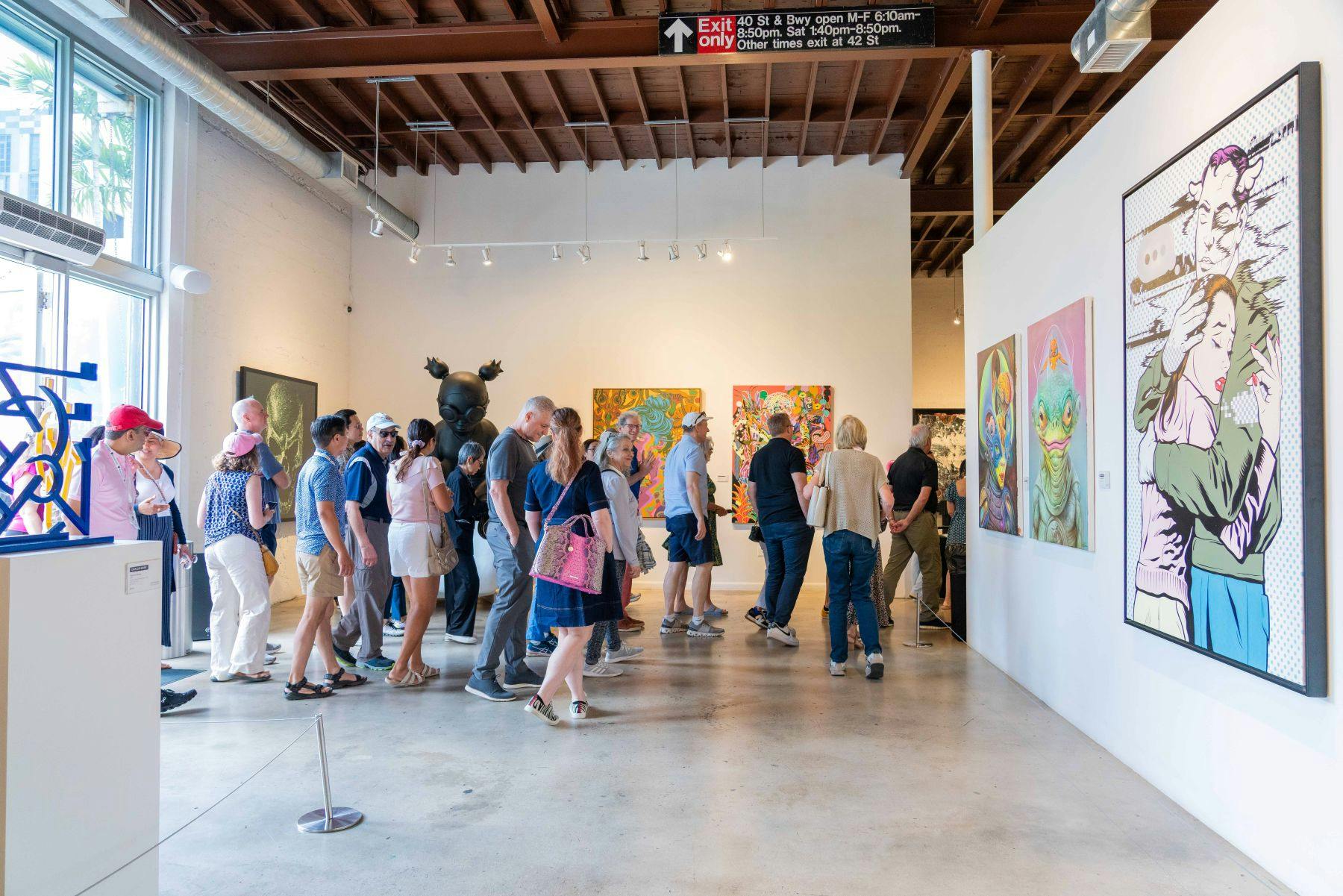 People viewing colorful artwork in a modern gallery with a wooden ceiling and white walls.