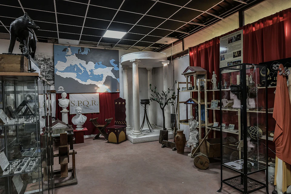 Exhibit room with Roman artifacts, including busts, pottery, a column structure, miniatures, and a large map of the Roman Empire.