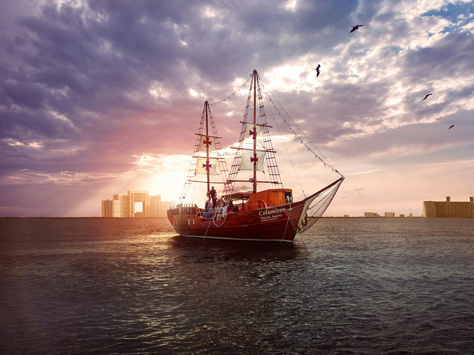 Una nave pirata rossa naviga sull'acqua al tramonto con edifici in lontananza e uccelli che volano sopra la testa.