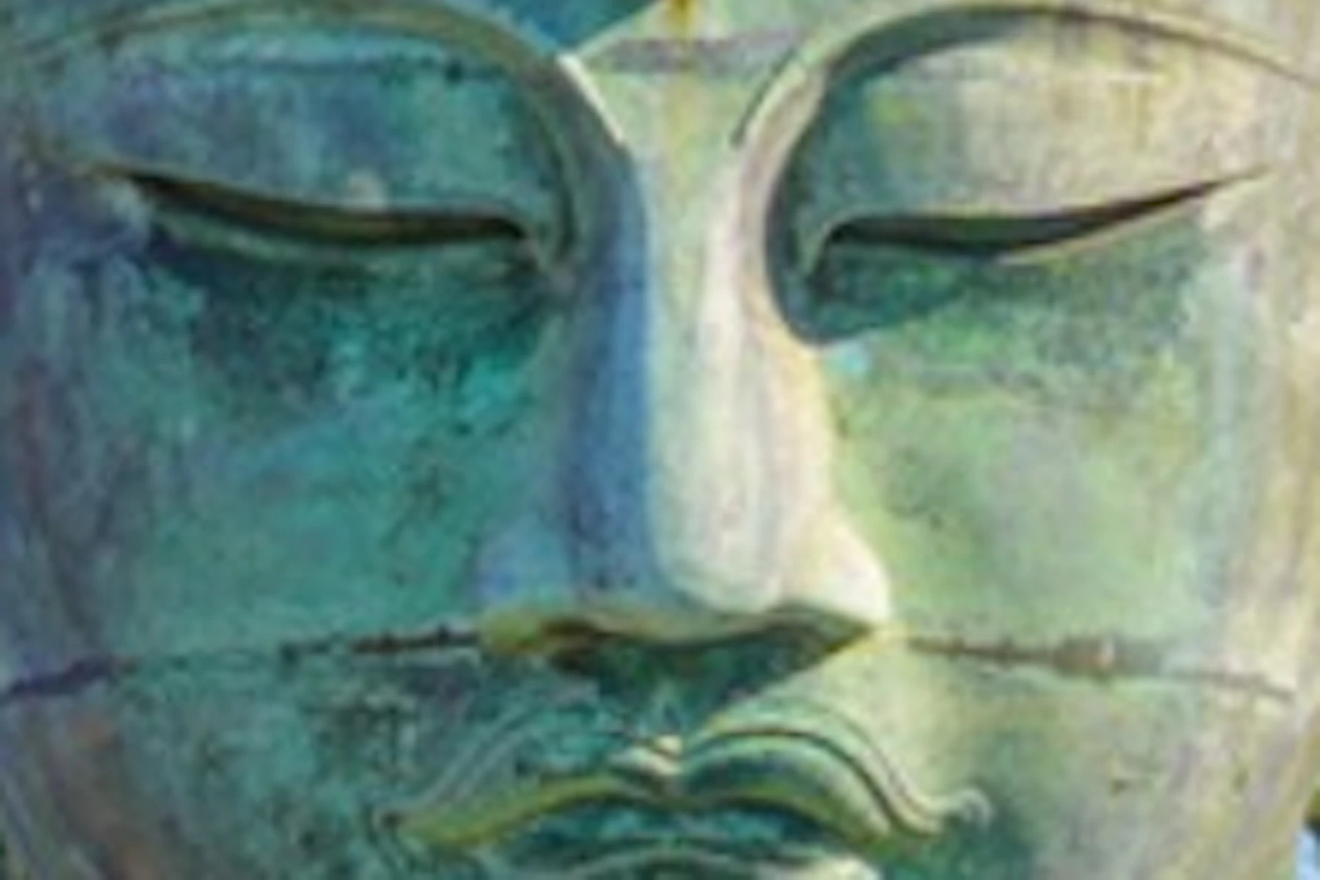 A large Buddha statue outdoors with people gathered in front of it, surrounded by greenery under a clear blue sky.
