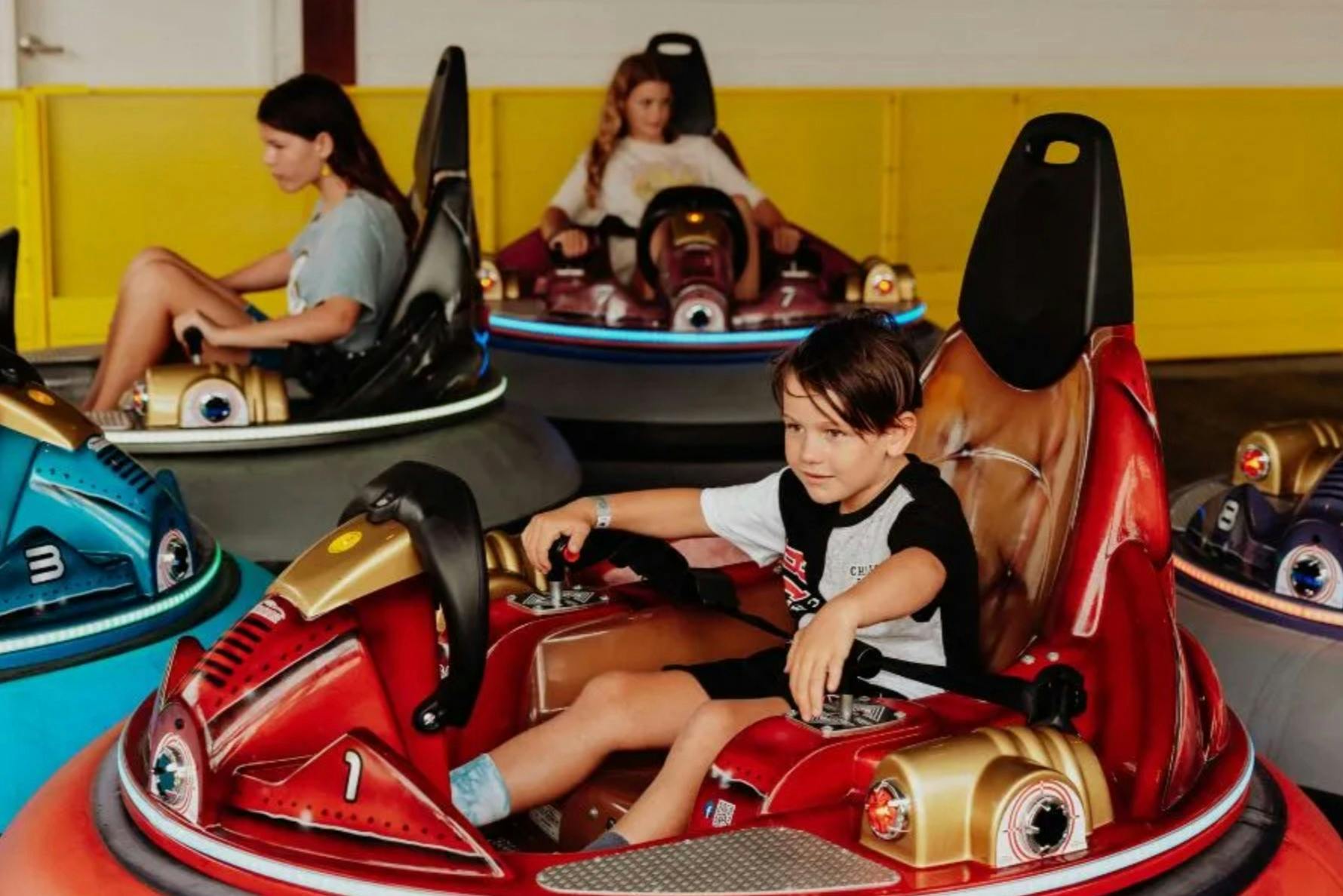 Children riding colorful bumper cars in an indoor amusement space.