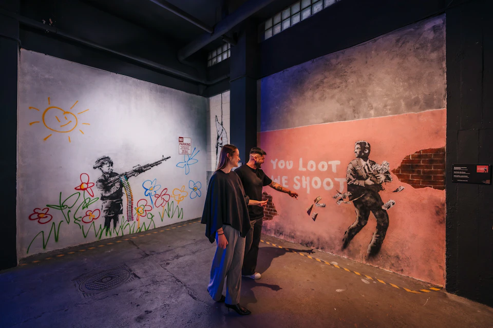 A couple smiling at a Banksy mural.