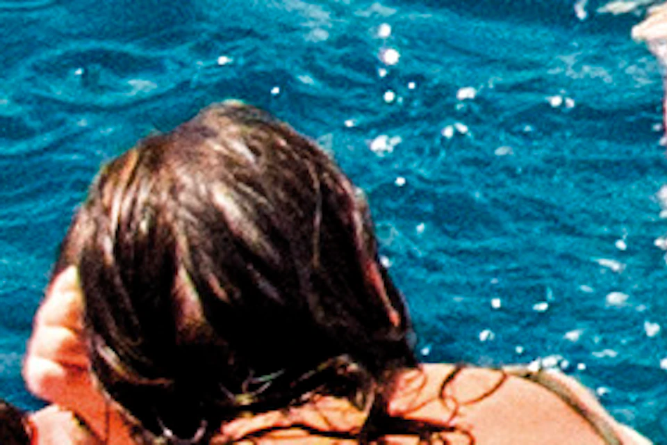 A group of people enjoying the sun on inflatable rafts and swimming in clear blue water near rocky cliffs.