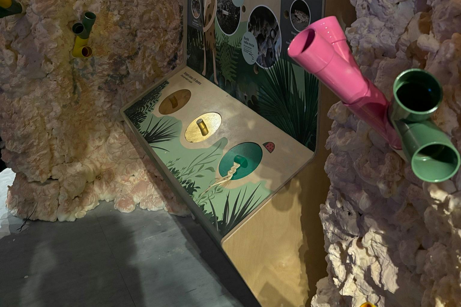 互动展览，色彩缤纷的管子和带有插入物体孔的面板，设置在洞穴般的环境中。