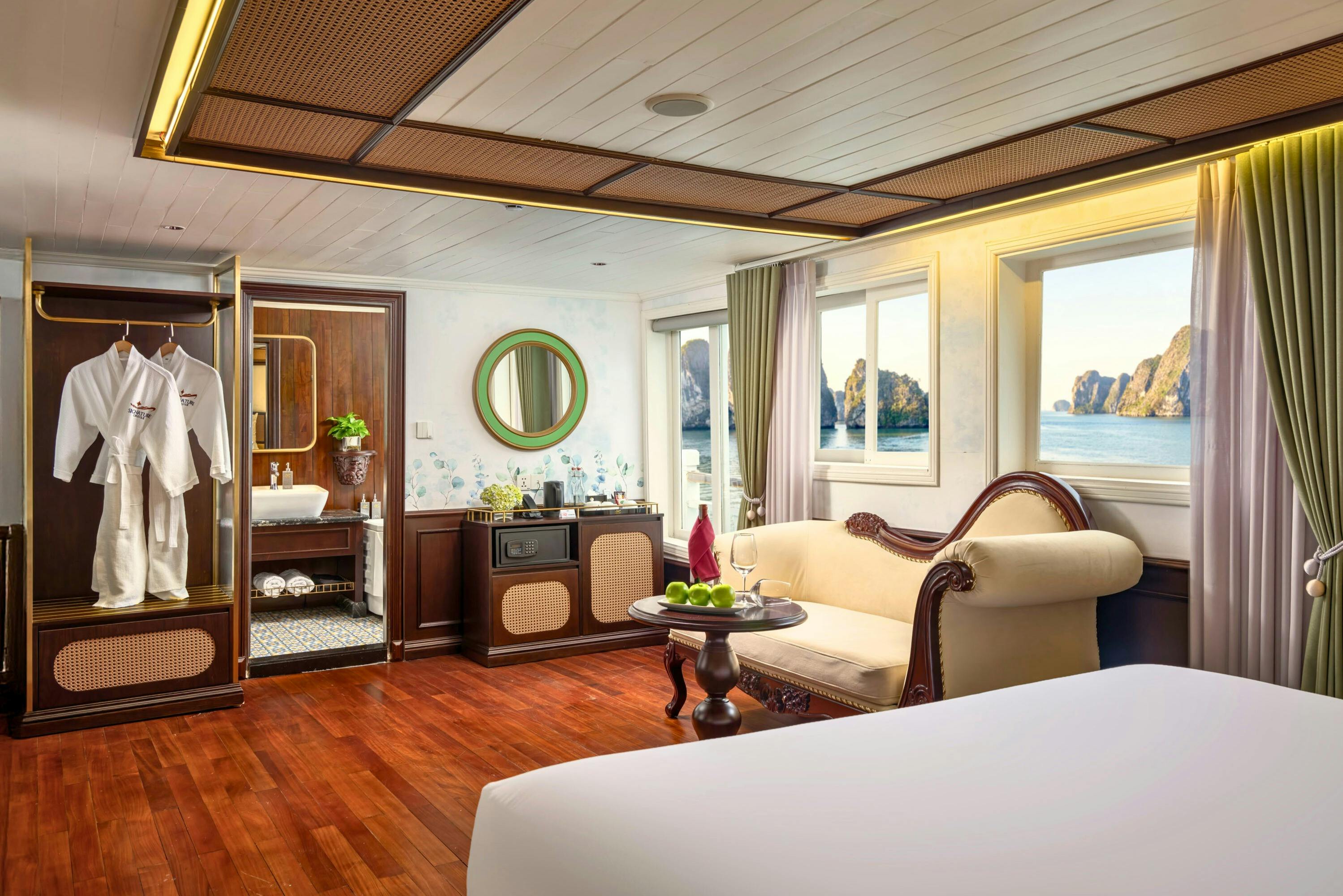 A cozy room with a large window view of a seascape, featuring elegant furniture, a bed, a sofa, a table, and a bathroom.