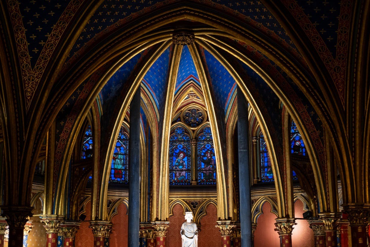Gothic cathedral interior featuring pointed arches, ornate stained glass windows, and a statue on a pedestal.