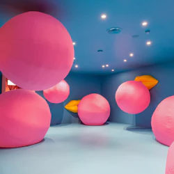Ett blåväggigt rum fyllt med stora rosa uppblåsbara föremål med gula basfästen och takspotlights.
