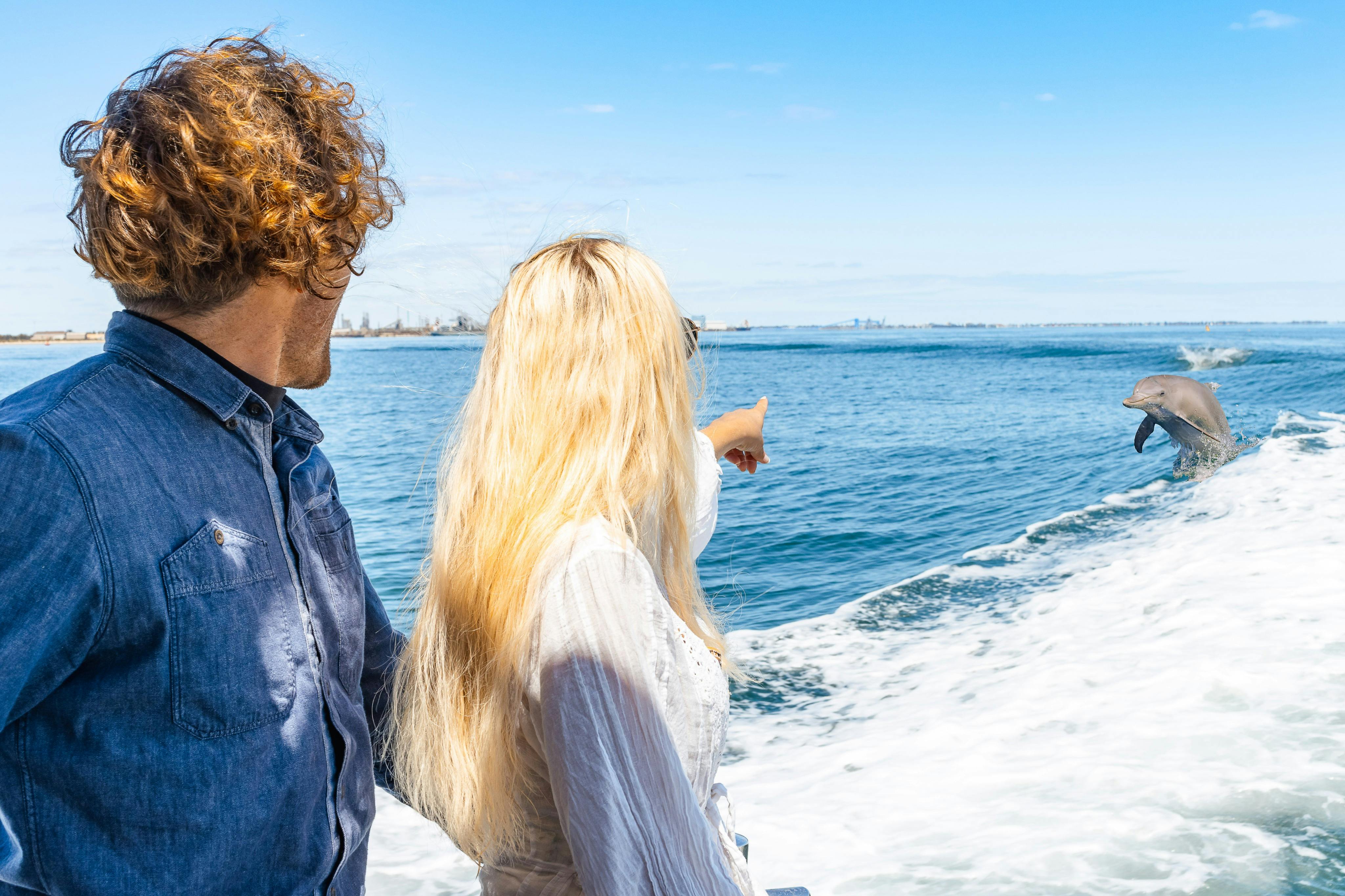 Δύο άνθρωποι στέκονται σε μια βάρκα, με τη γυναίκα να δείχνει προς τον ορίζοντα πάνω από ένα σώμα νερού κάτω από έναν καταγάλανο ουρανό.