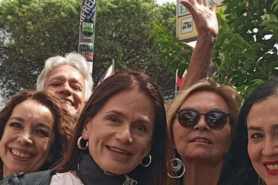 A group of six people smiling and posing in front of a sign that reads 'Pompeii,' with trees and greenery in the background.