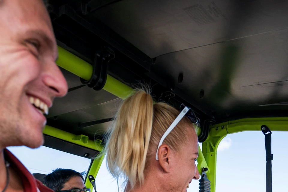 Three people sitting in an open vehicle, two smiling and one shaking hands with a standing person outside the vehicle.