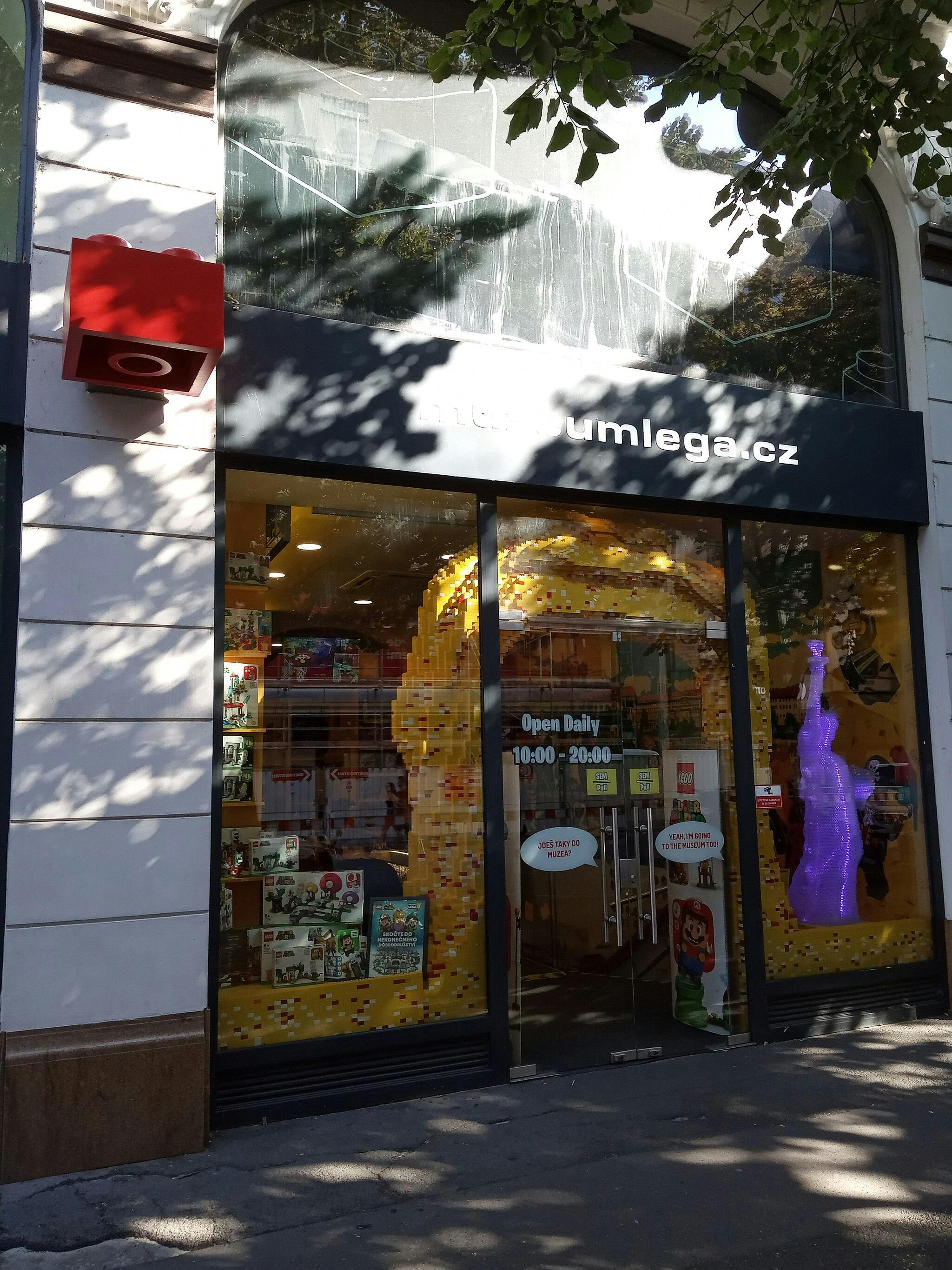 Výkladní skříň s nápisem „museumlega.cz“ s motivem LEGO a fialovou sochou LEGO uvnitř.