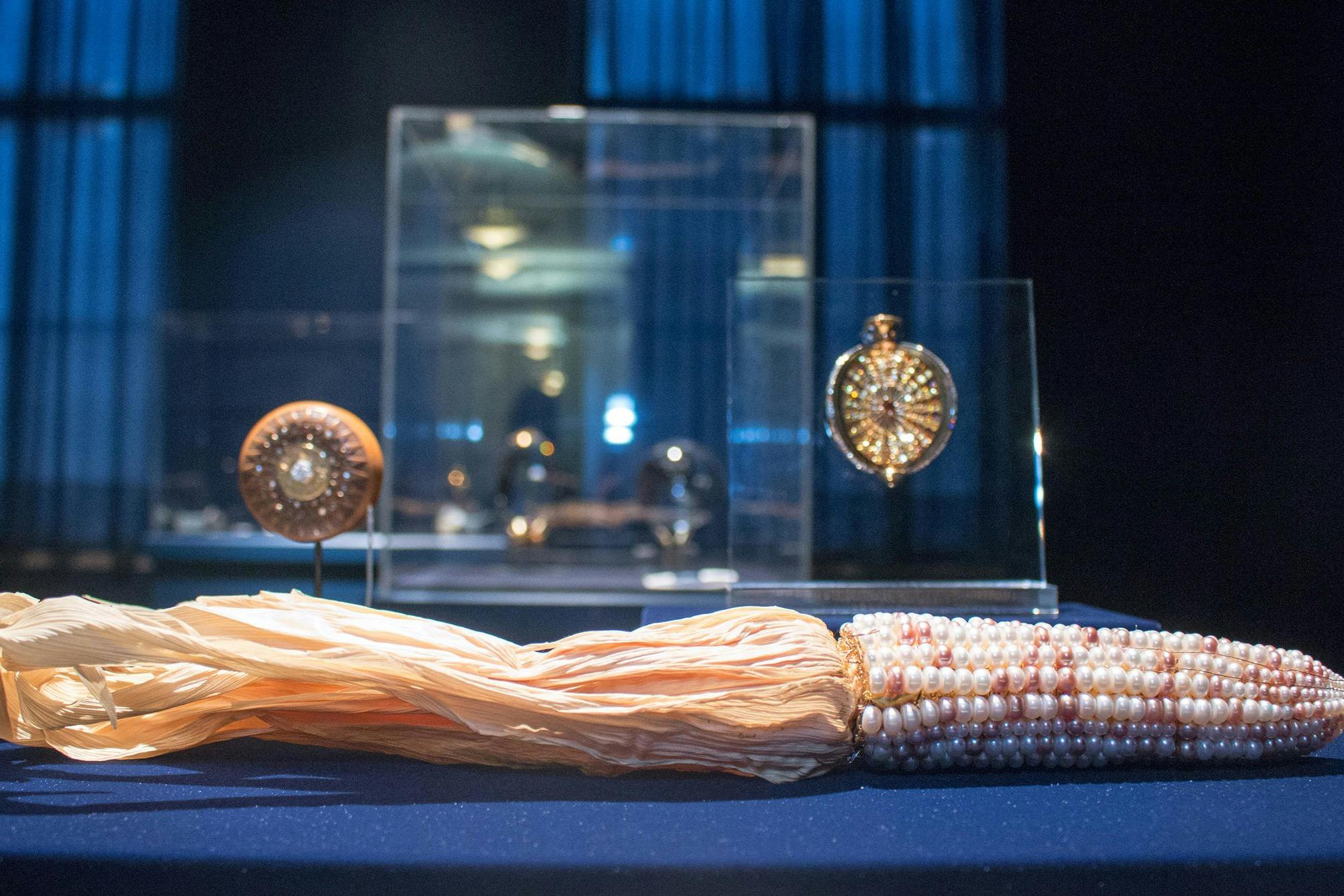 A collection of ornate jewelry displayed in glass cases, with a pearl and tassel necklace in the foreground on a blue surface.