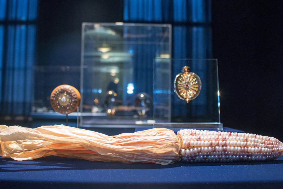 A collection of ornate jewelry displayed in glass cases, with a pearl and tassel necklace in the foreground on a blue surface.