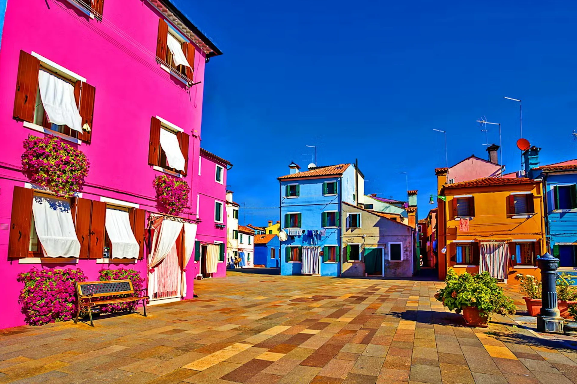 A vibrant square with colorful houses in shades of pink, blue, and orange under a clear blue sky.