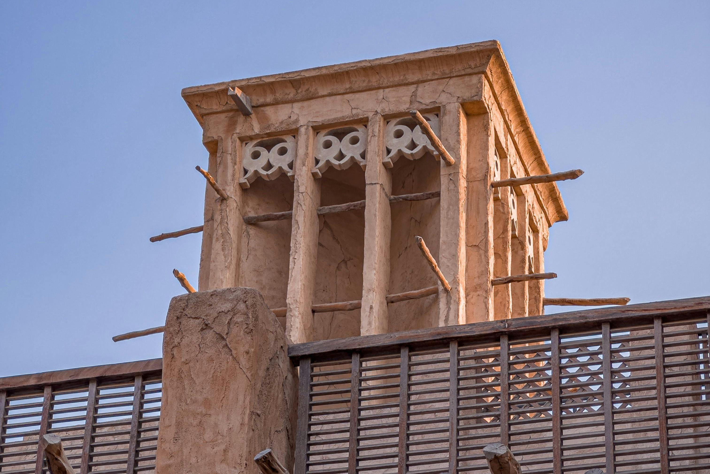 A traditional wind tower with wooden protrusions and decorative elements, seen against a clear blue sky.