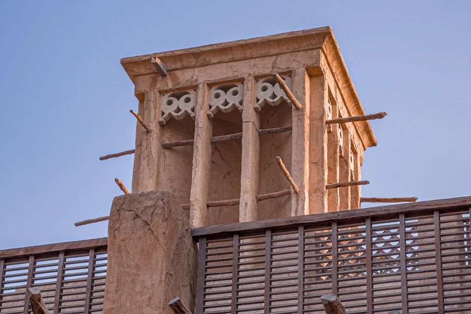 A traditional wind tower with wooden protrusions and decorative elements, seen against a clear blue sky.