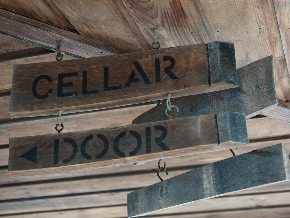 Hanging wooden signs under a wooden ceiling with the words "CELLAR" and "DOOR" painted in black.