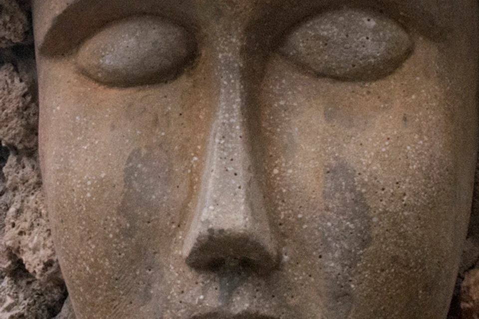 Close-up of a stone sculpture with a serene face and textured hair, surrounded by rock formations and foliage.