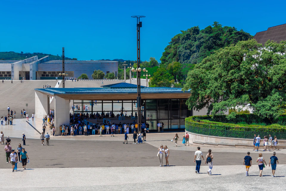 A group of people gathered near a modern building surrounded by greenery, with a few individuals walking in the foreground.