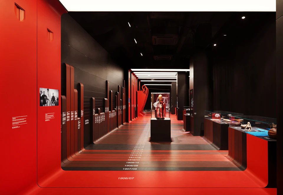 Exhibit hall with red and black decor, featuring historical timelines on the walls and sports memorabilia display cases.