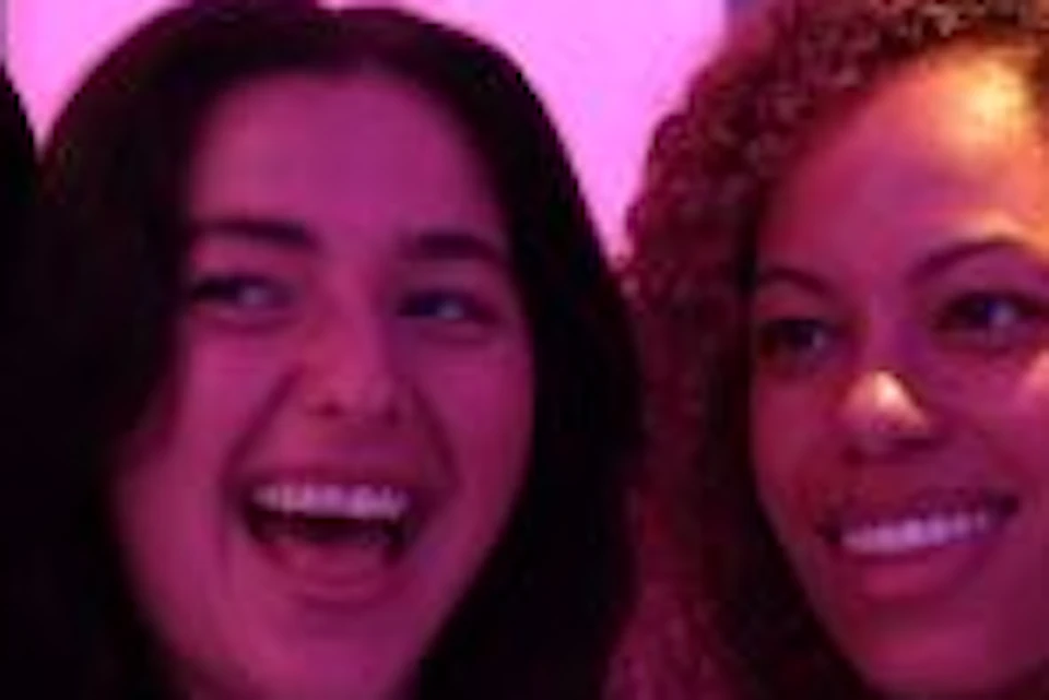 Four people smiling and taking a selfie surrounded by glowing, colorful hanging spheres in a dark room.