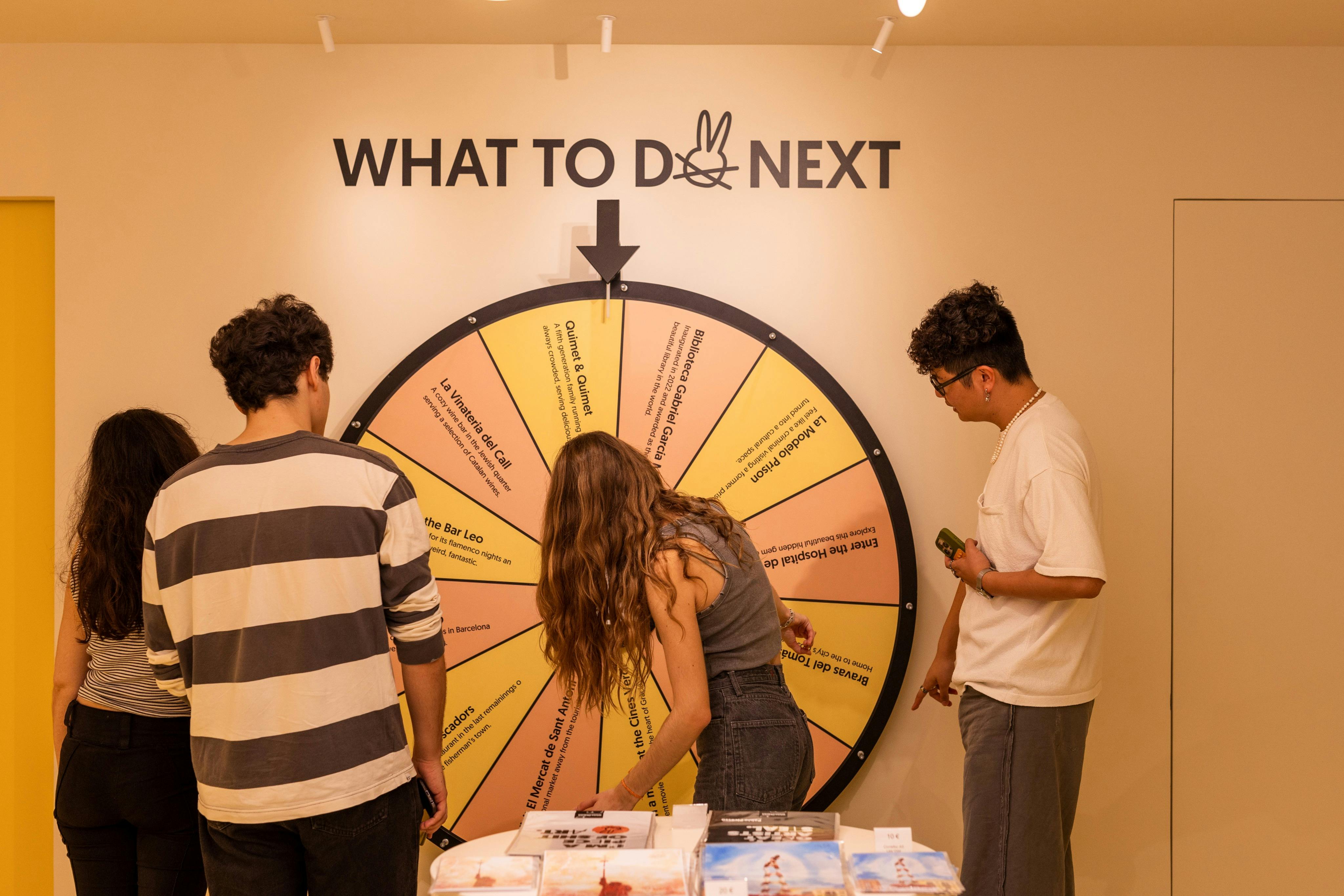 Trois personnes se tiennent autour d'une grande roue "Que faire ensuite ?", pointant du doigt et examinant les options qui y sont inscrites.