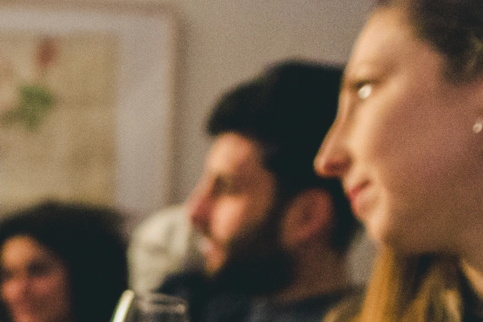 Three bottles of port wine on a table; blurred background of people talking and one person holding a glass.
