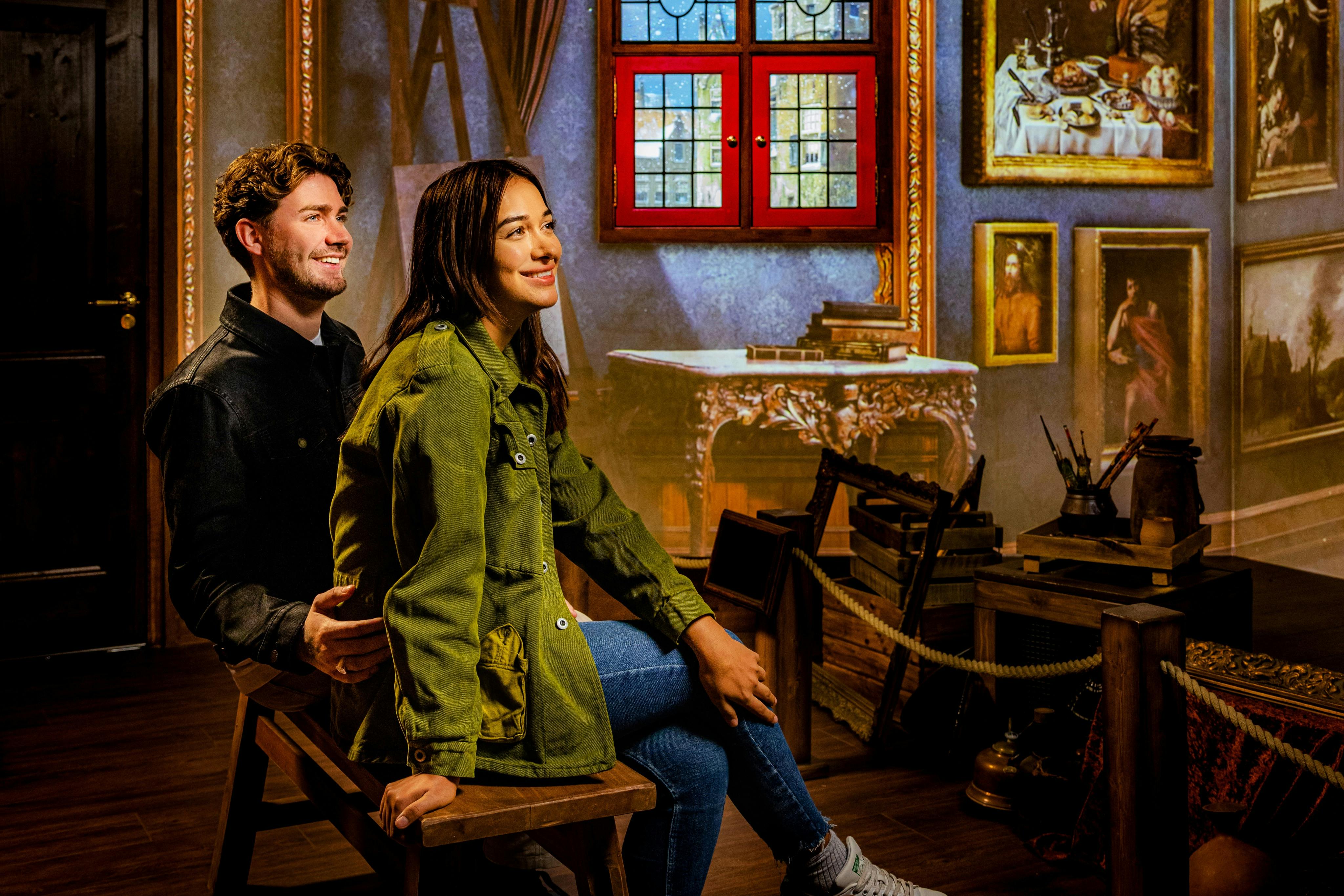 나무 바닥, 장식 벽, 스테인드글라스 창문이 있는 따뜻하고 소박한 방에 한 남녀가 나무 벤치에 앉아 있습니다.