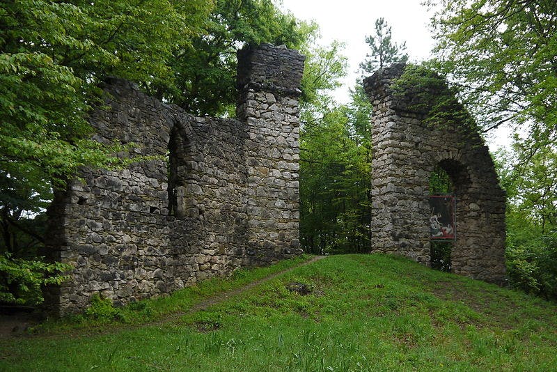 Ruines en pierre d'une ancienne structure au milieu de la verdure, avec deux grandes arches en pierre et des vestiges de murs.