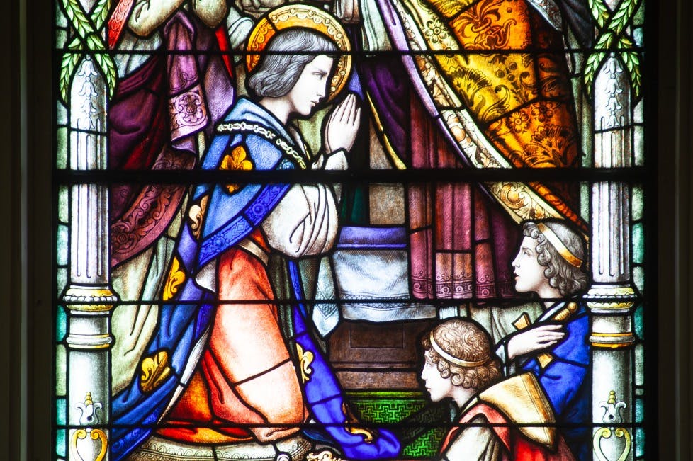 Περίπλοκο βιτρό παράθυρο που δείχνει τρεις φιγούρες με φωτοστέφανα, στολισμένες με ζωντανές ρόμπες, που ασχολούνται με μια θρησκευτική σκηνή.