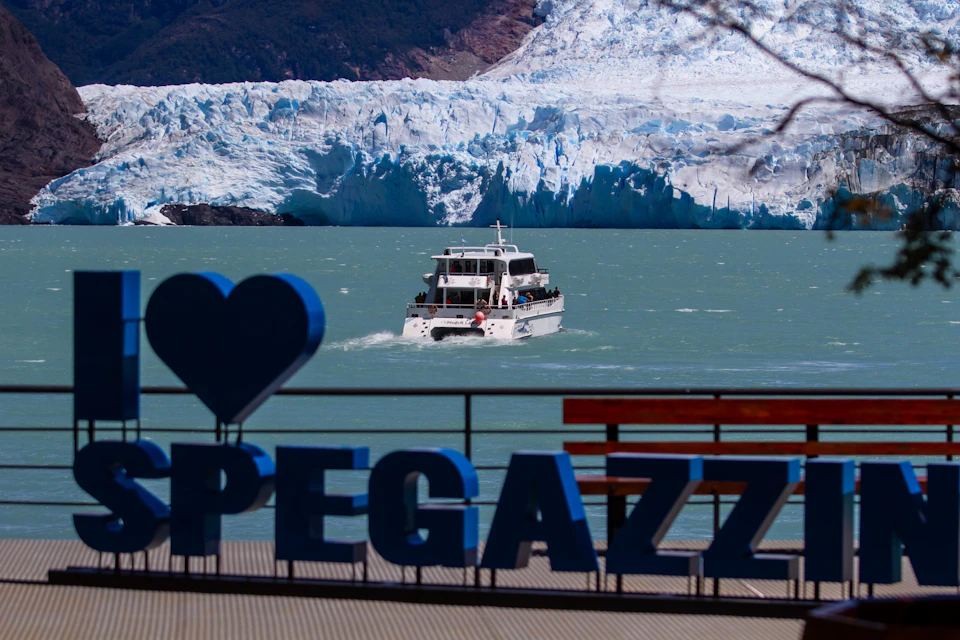 A tour boat on a turquoise lake near a glacier, with a blue sign reading 'Pegazz' in the foreground.