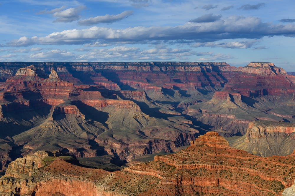 Expansive view of the Grand Canyon with layered red and orange rock formations under a partly cloudy sky.