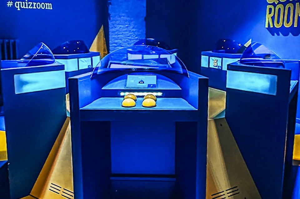 A museum exhibit featuring yellow shoes displayed under a transparent dome, surrounded by interactive displays in a blue-lit room.