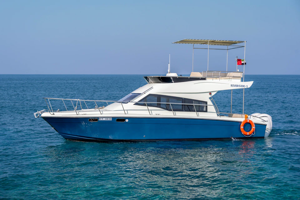 A blue and white motorboat named 'Riverside-1' floating on calm blue water under a clear sky.