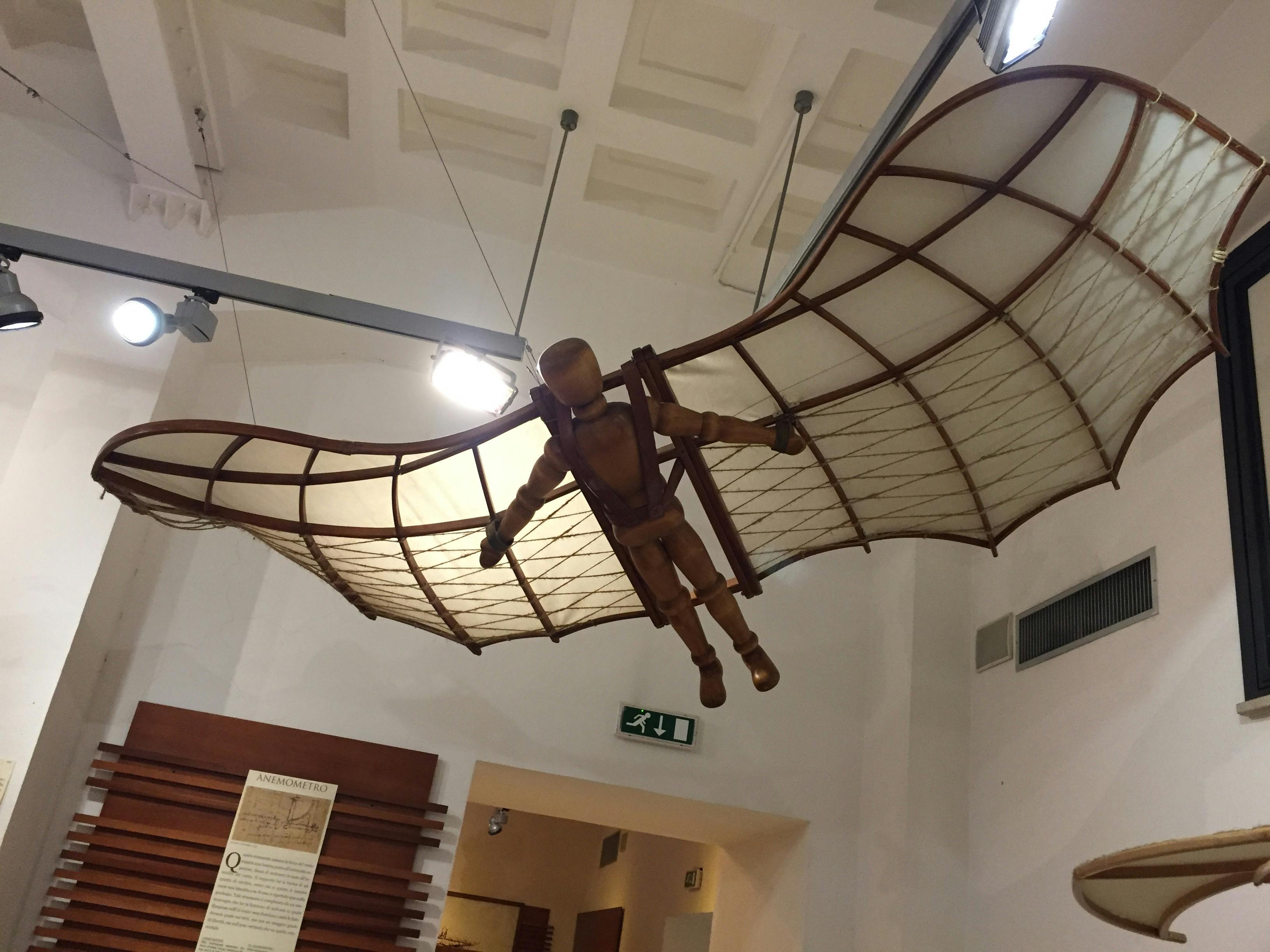 A wooden mannequin with wings modeled after Da Vinci's flying machine hangs suspended in a museum setting.