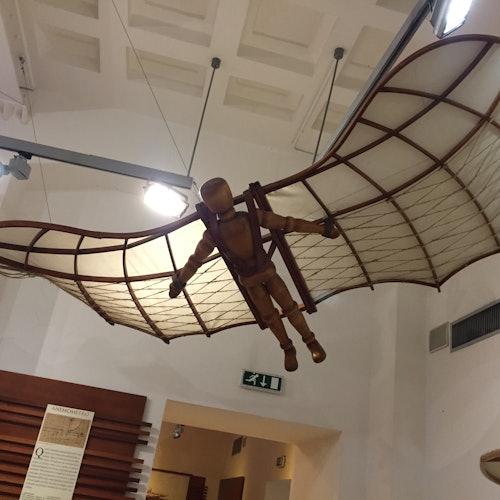 A wooden mannequin with wings modeled after Da Vinci's flying machine hangs suspended in a museum setting.