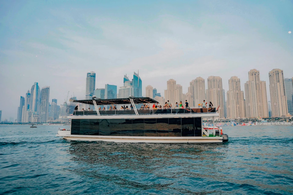 A boat filled with people cruising on water with a city skyline of tall buildings in the background.