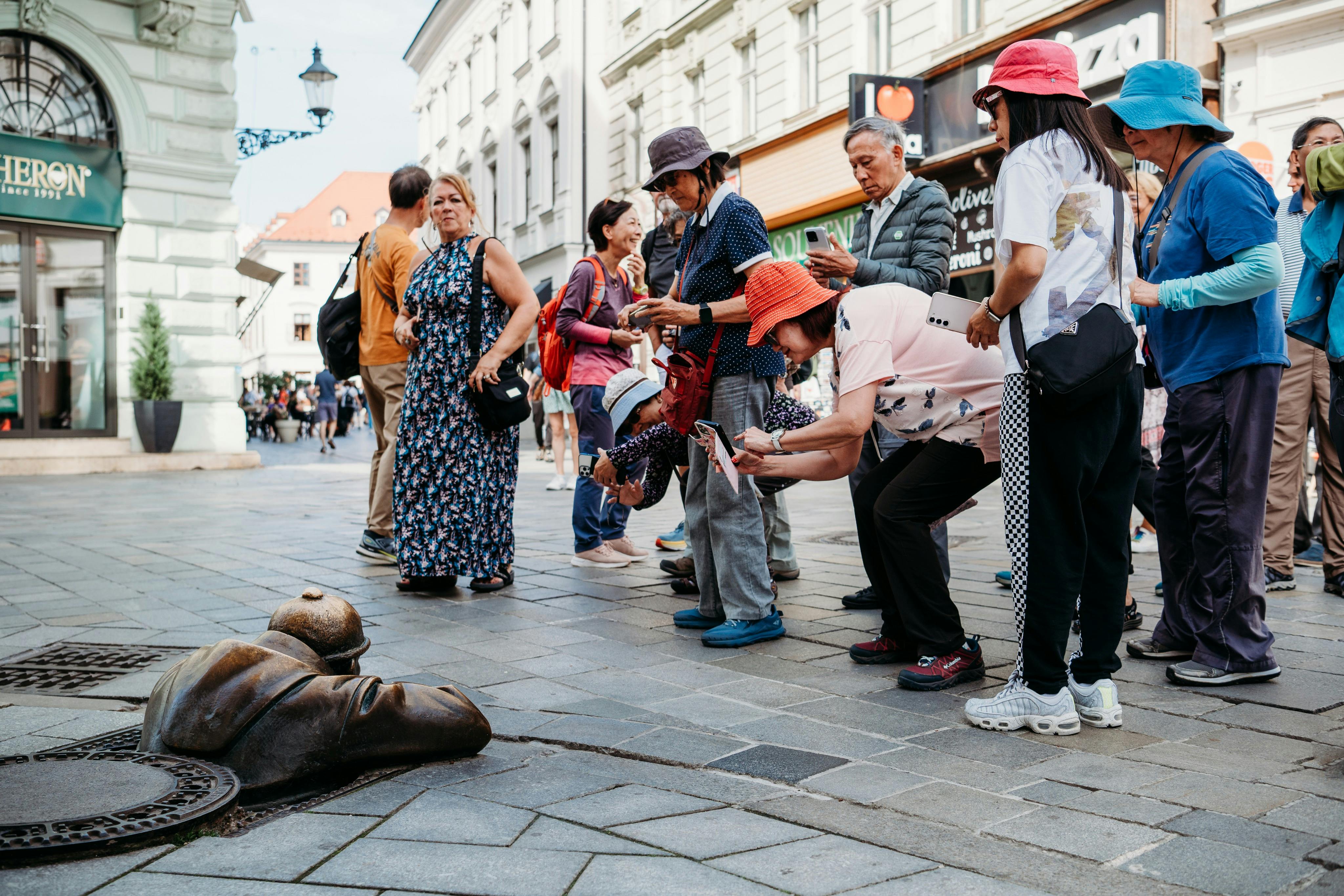 游客在城市街道上观察并拍摄一尊从人孔中出来的男子青铜雕像。