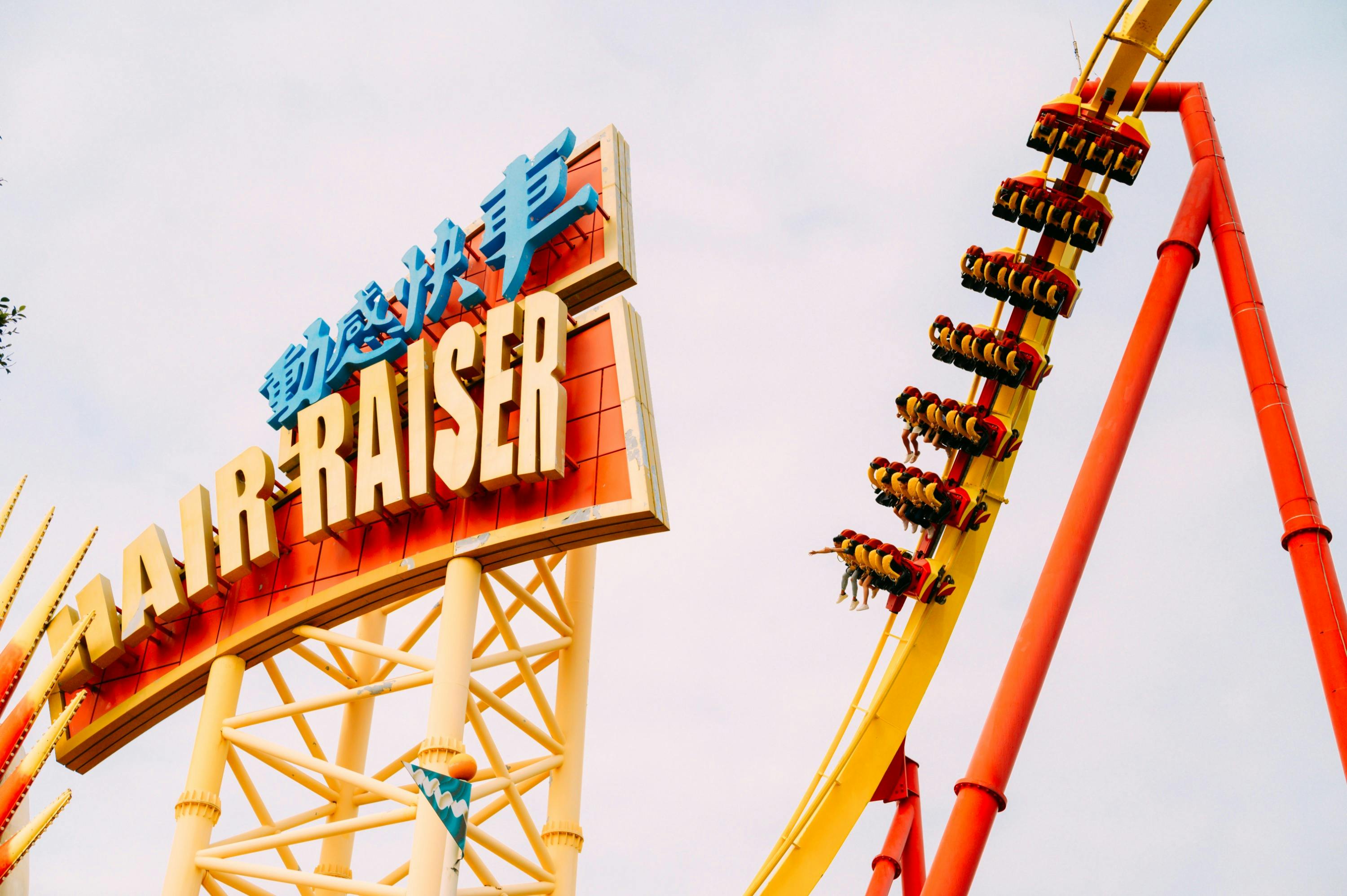 A roller coaster with a steep yellow track and riders in a loop, next to a colorful sign featuring characters and letters.